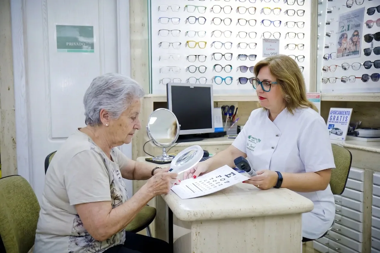 Una óptico-optometrista muestra una lupa de mano a una paciente mayor durante una consulta de baja visión