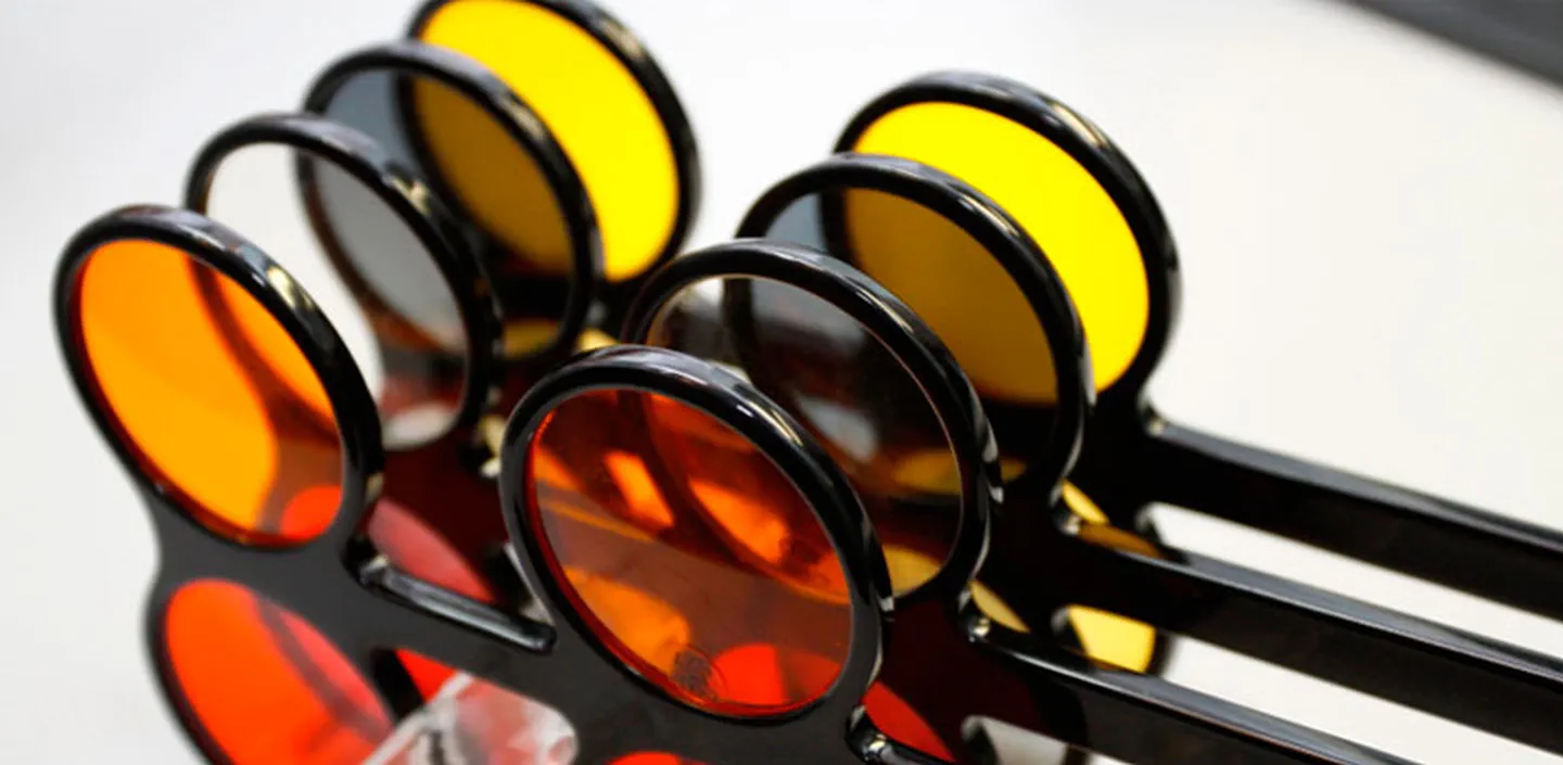 Varias gafas con filtros de color ámbar, naranja y rojo apiladas sobre fondo oscuro