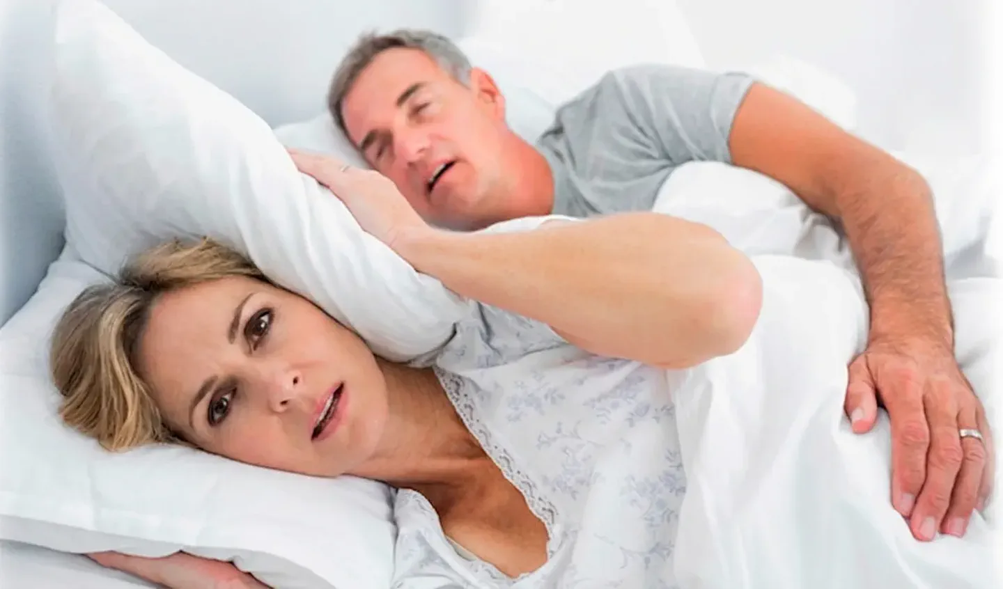 Una mujer se tapa los oídos con la almohada mientras el hombre que duerme a su lado ronca